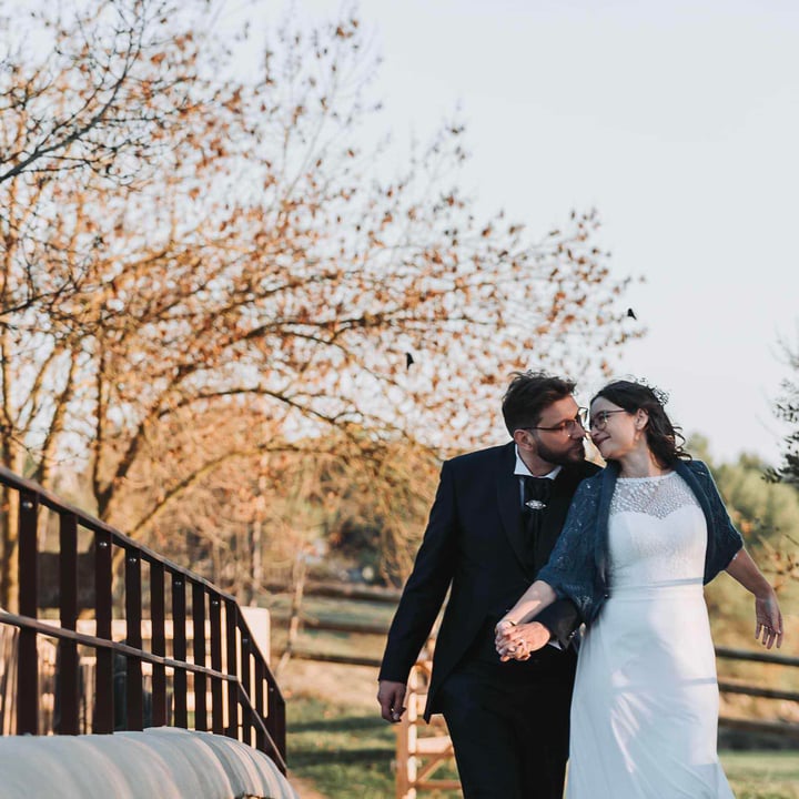 Un couple de mariés se tenant par la main sur un pont, entouré d'arbres aux feuilles dorées, avec une lumière douce du matin, créant une atmosphère romantique et chaleureuse idéale pour un photographe de mariage.